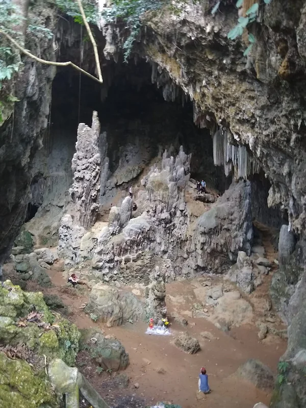 A cave in Vietnam. Stalactites drip from the ceiling. Stalagmites grow in a mountain that several figures are climbing.