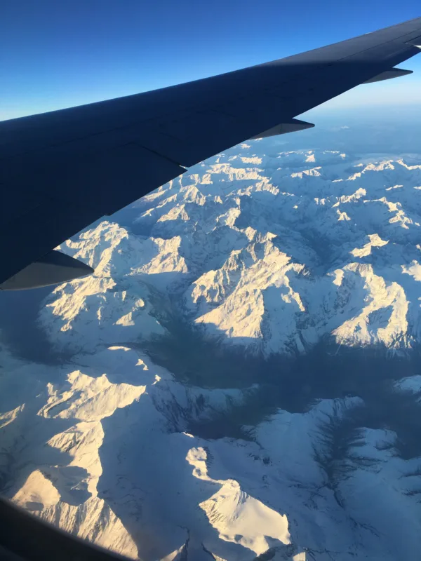 View from a plane: a dark wing cuts over icy mountains in the Alps
