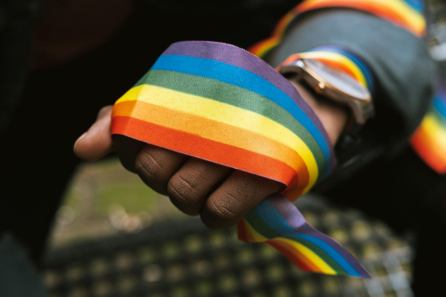 A close-up of a Black person's hand wrapped in a rainbow ribbon.