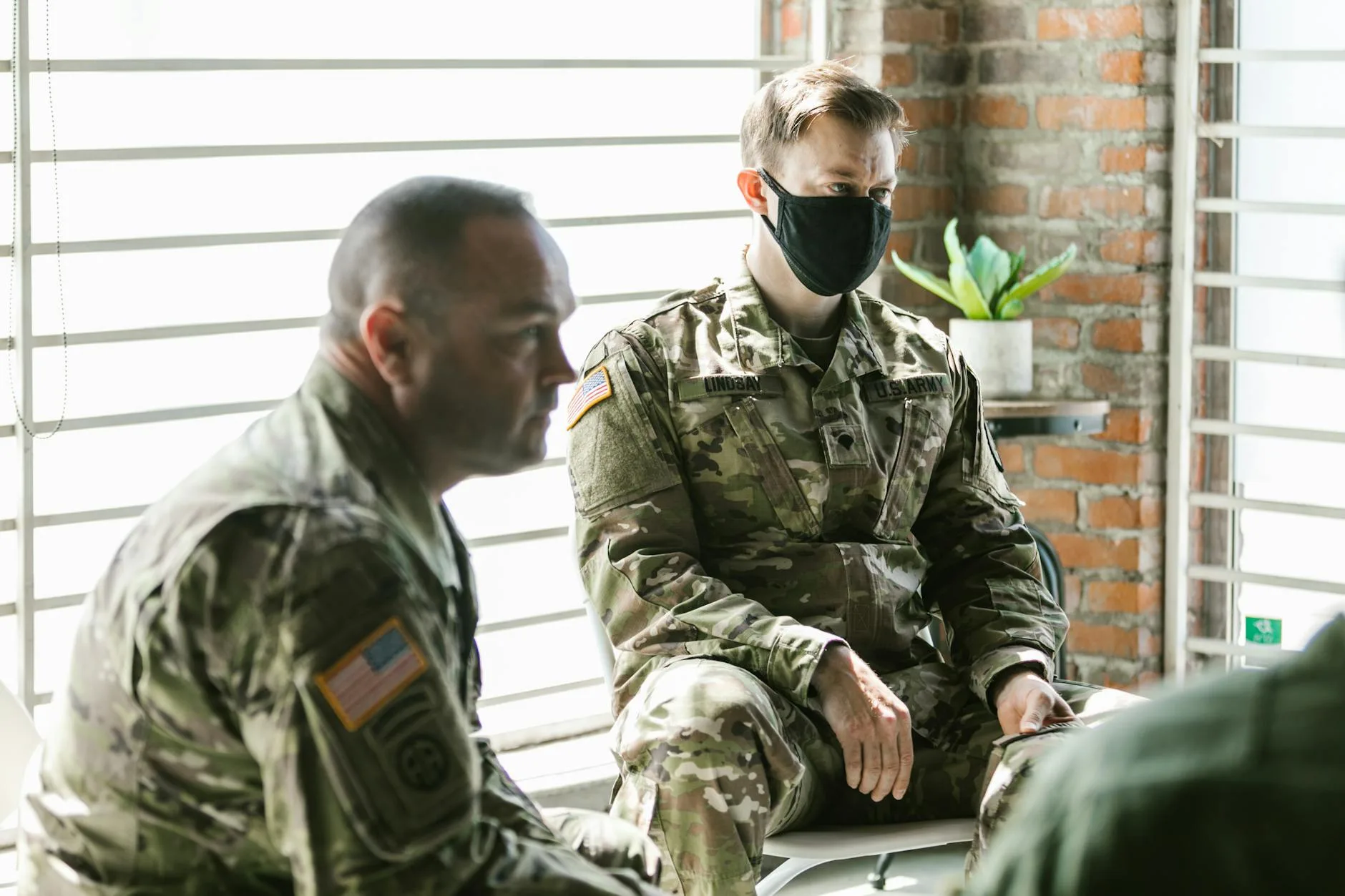 Two soldiers in camouflage uniforms, sitting in an office.