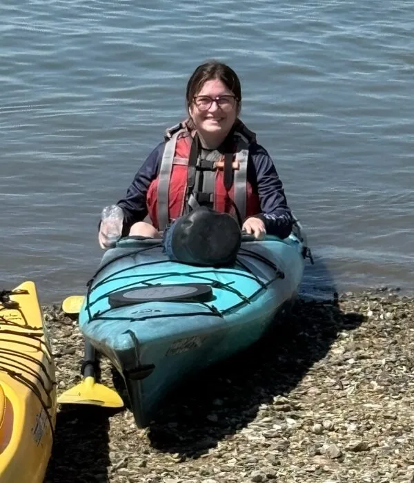 Deanna, a brown-haired white woman, sitting in a kayak at the edge of the marsh