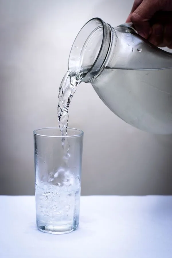 clear glass pitcher pouring water on clear drinking glass